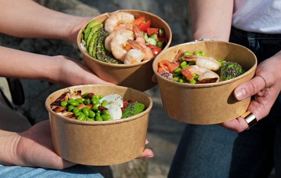 Three people holding up food bowls with beans, avocado and shrimp.